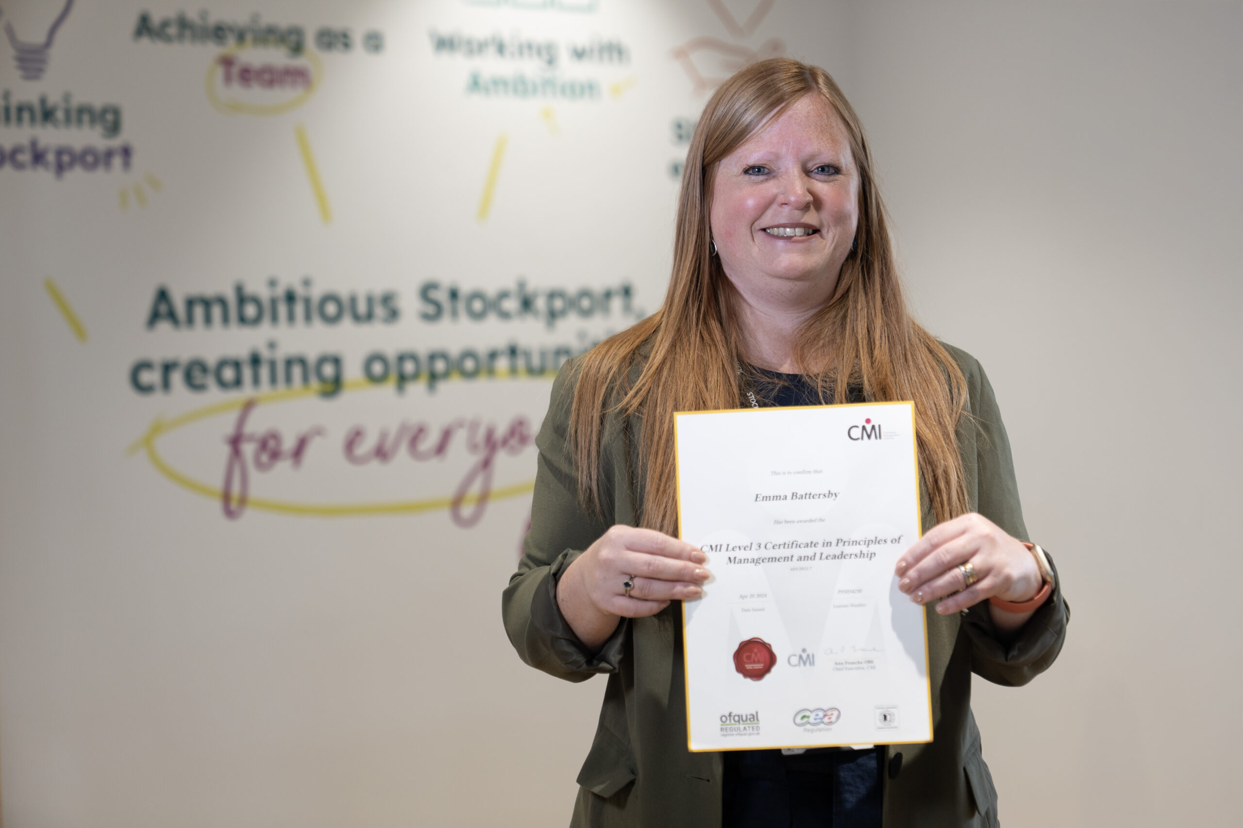 Person holding a certificate in front of a wall with motivational text about ambition and opportunity.